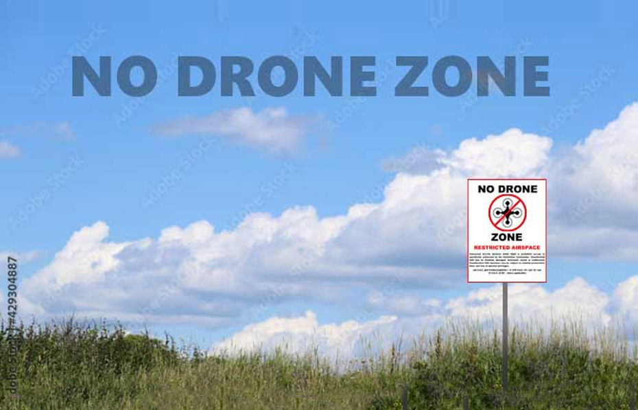 View of a grass field, blue sky, with sign that says No Drone Zone